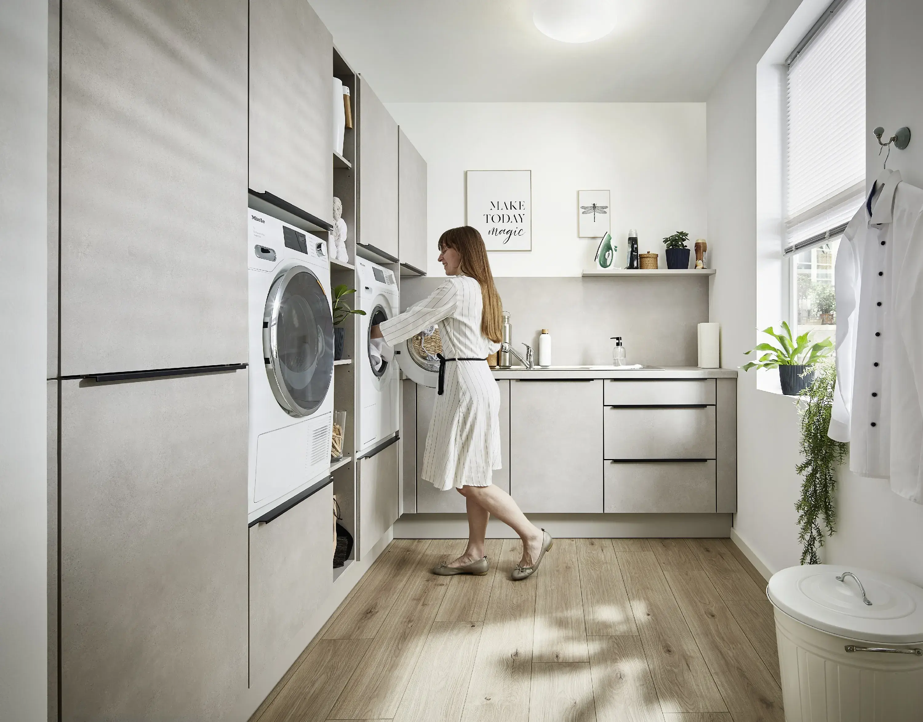ergonomisch erhöht nebeneinander eingebaute Waschmaschine und Trockner Frau im Morgenmantel legt Wäsche in den Trockner